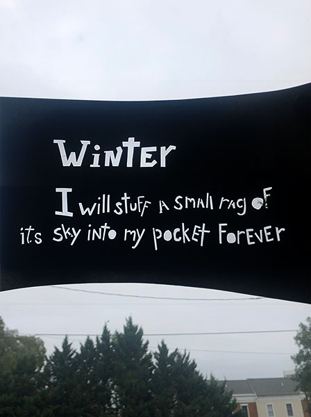 A stencil showing text from “Winter” by Larry Levis. Held up against the sky.