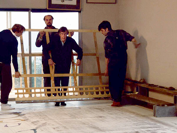 John Cage (center) assisted inside the framework of a 56 inch wide custom-made brush
