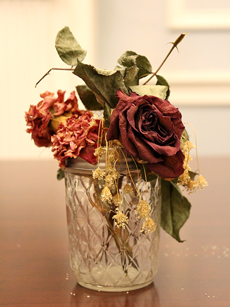 Dried red roses, carnations, and white baby's breath in an empty jam jar