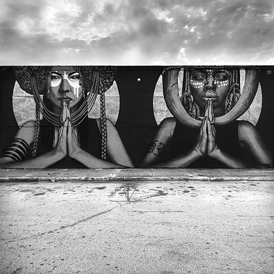 Photograph of street art of two women side by side with prayer hands.