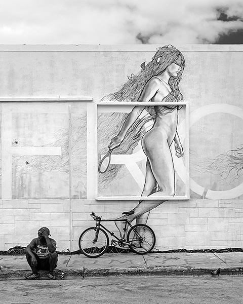 Photograph of street art of a woman. Bicycle and man in foreground.