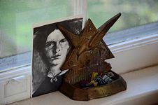 Postcard portrait of Emily Dickinson held up by metal bookend with a spread winged bird against a triangle and foward attached tray holding multi-color spring clips.