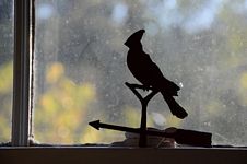 Silhouette of a perched cardinal weathervane in front of window.