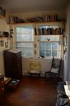 Shot showing dictionary stand, high mounted books shelves in front of windows, and rocking chair.