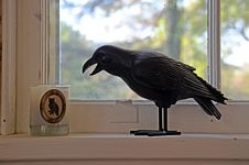 Crow figurine, open beak, facing a glass with an owl emblem.