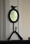 Oval mirror topped with a bird, hook at bottom with leather bag hanging.