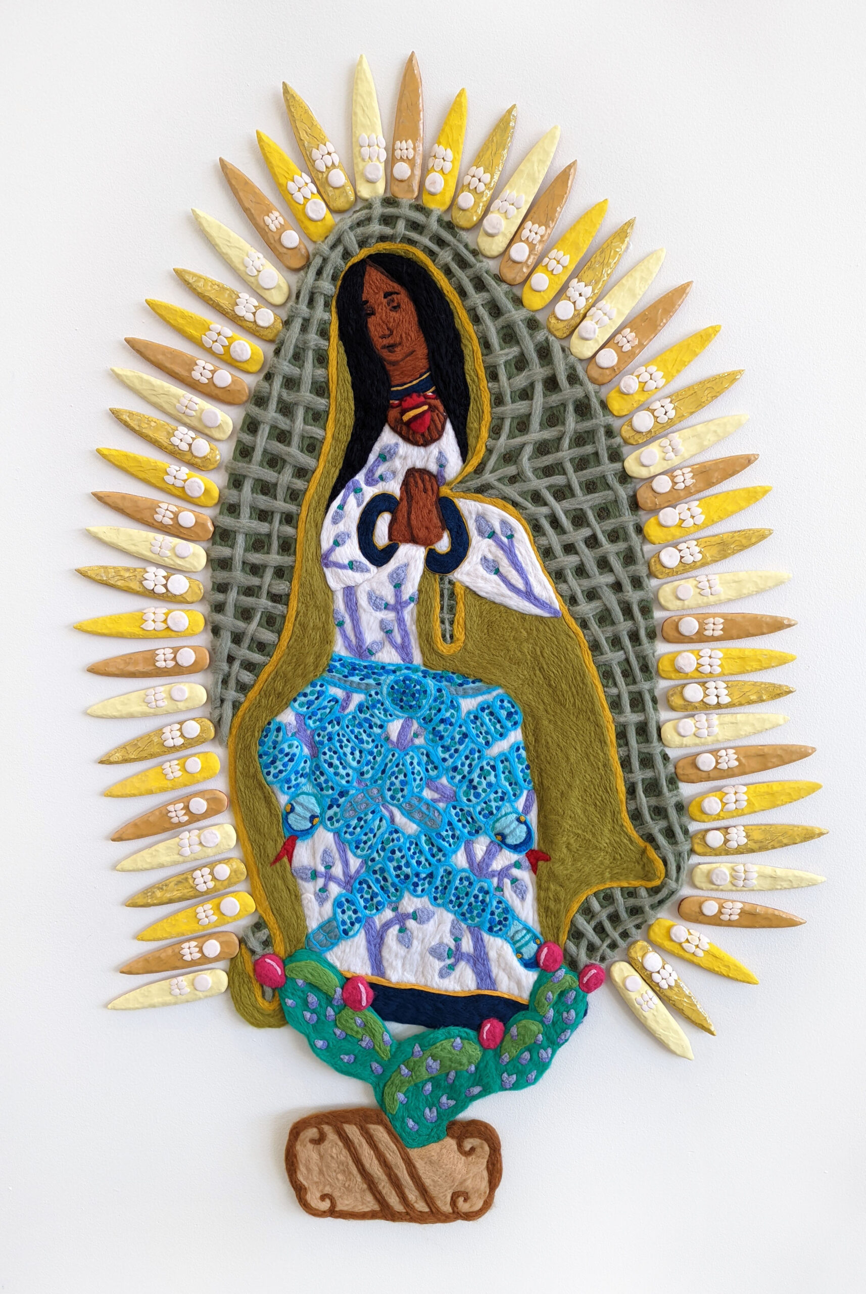 A felted sculpture of the Mexica goddess Coatlicue represented as the Virgin Mary, surrounded by ceramic macuahuitl.