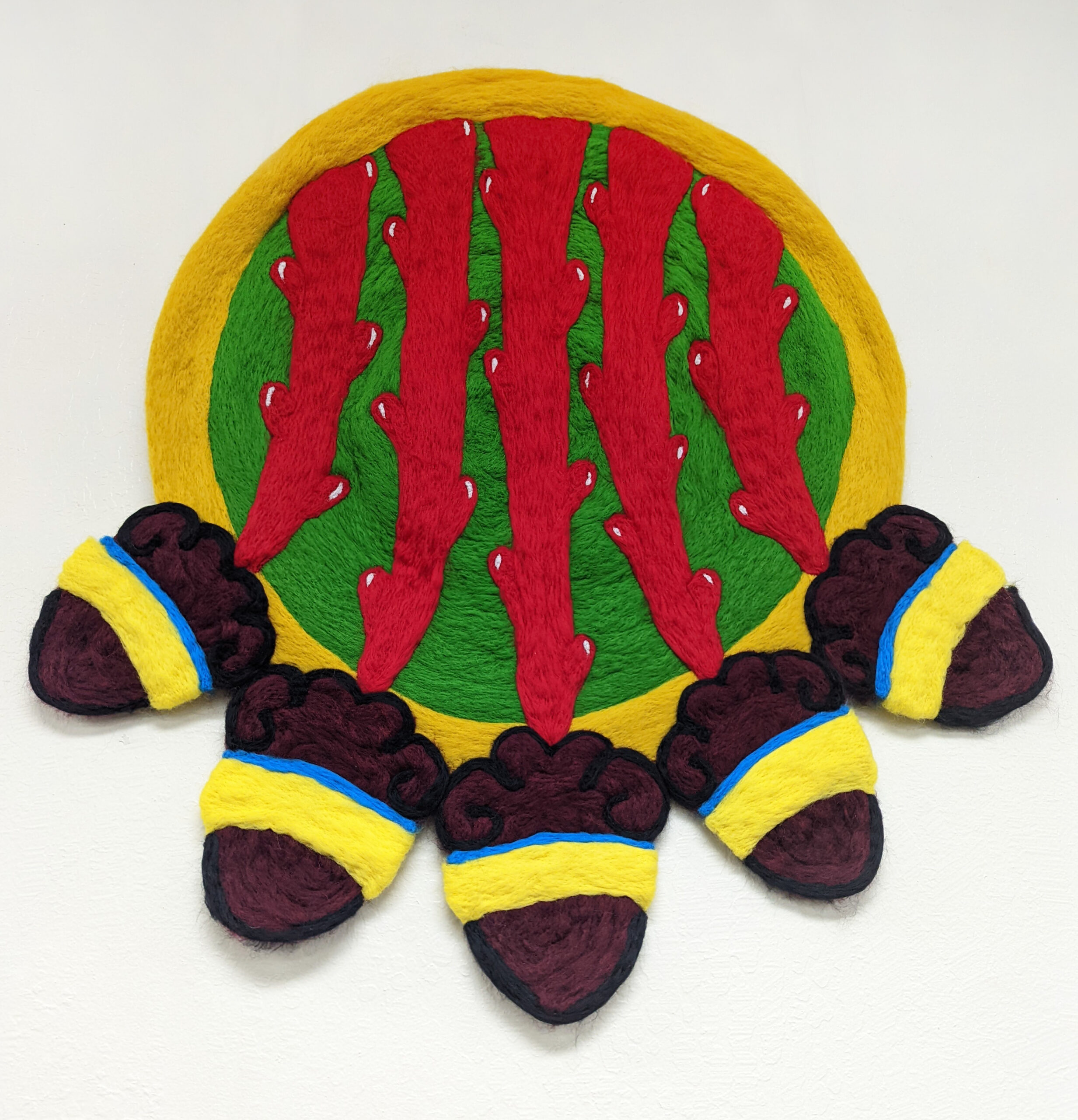 A felted wool sculpture of an Aztec shield featuring five hearts on a white background.