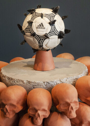 A concrete and ceramic sculpture of a Mexica tzompantli, a skull rack, with an obsidian encrusted soccer ball atop the altar.