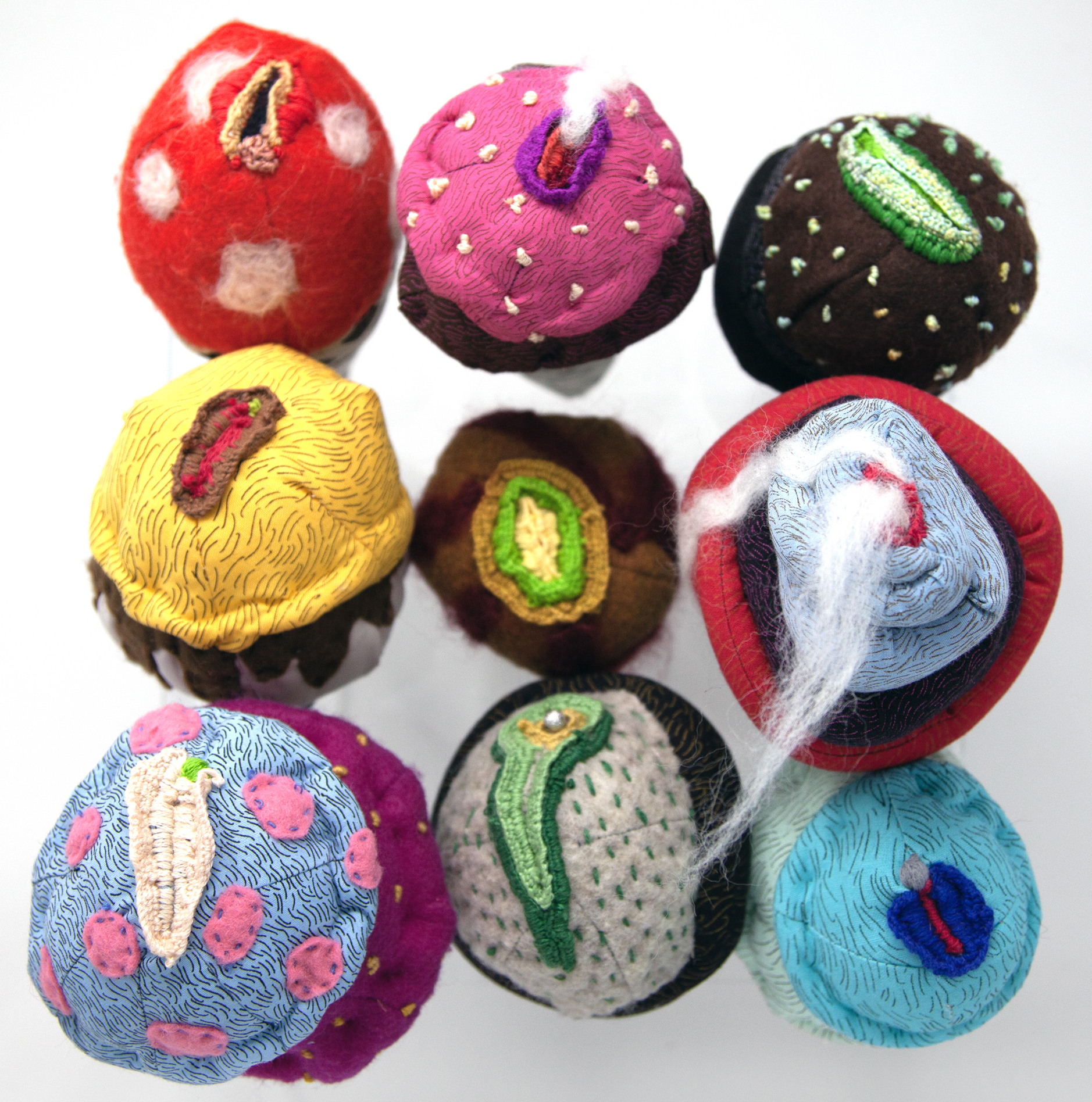 Nine soft-sculpture ice cream cones alluding to vaginas and made of various fabrics, pompoms, beads and accessories. Some of the fabrics are screen printed with patterns.