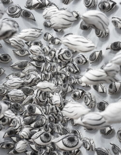 A gallery installation of hundreds of black and white, relief-printed, soft-sculpture eyes, some hanging and others attached the the gallery wall in a cluster.