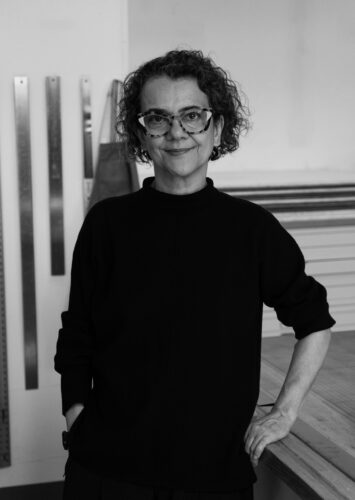 Artist Tanja Softic standing in her studio with tear bars hanging in the background.