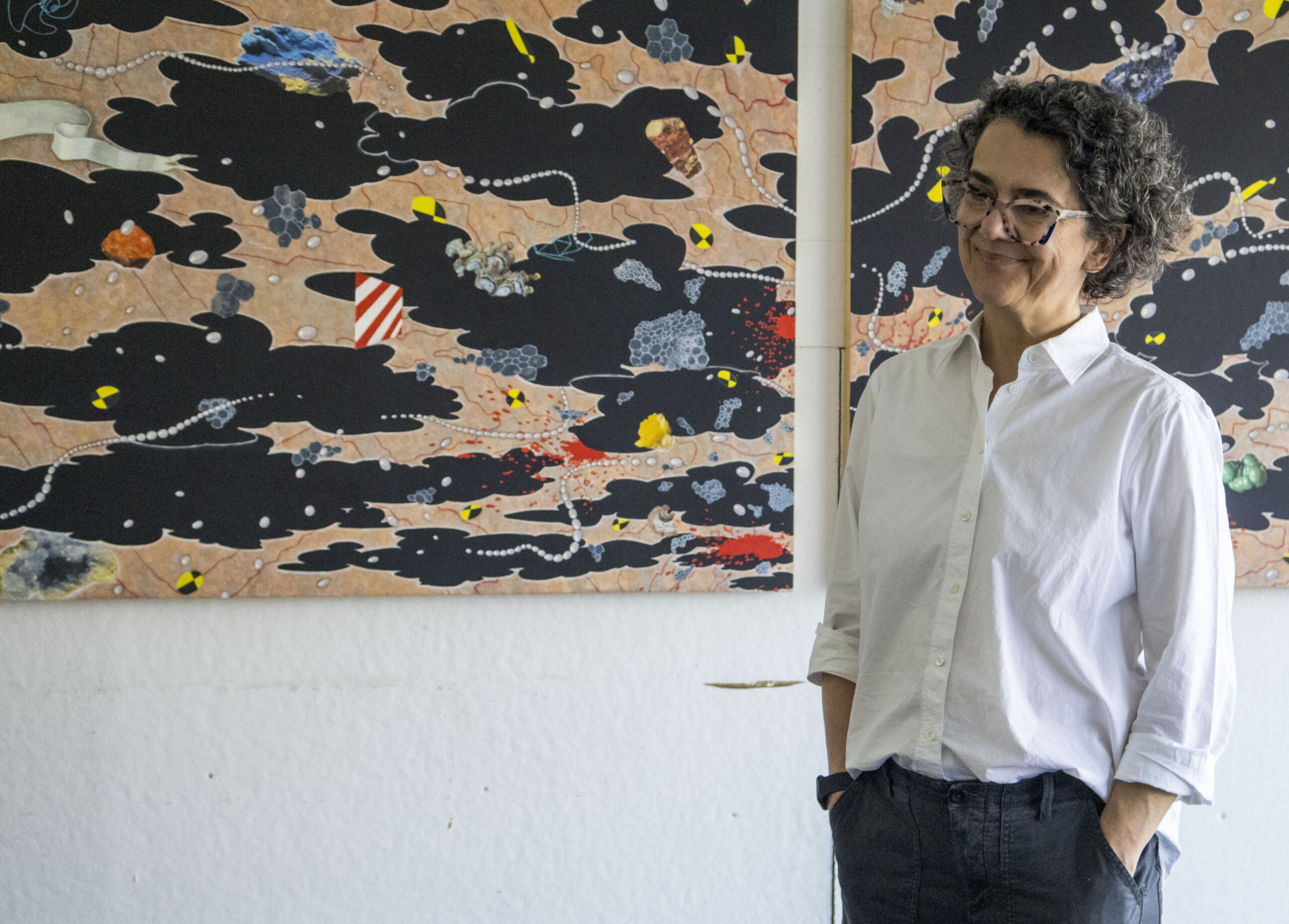 Artist Tanja Softic standing and smiling in front of two large panels of her artwork.