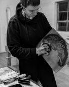 A grayscale photograph of artist Erin Wohletz wiping the ink from a copperplate in a printmaking shop.