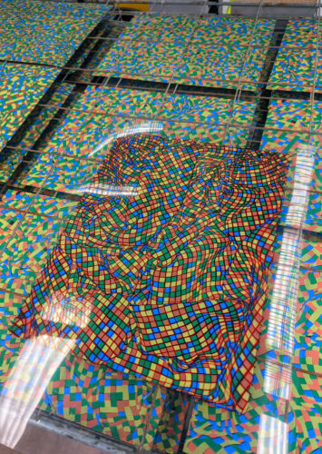 An edition of screenprints featuring multicolored checked fabric stacked on a drying rack.