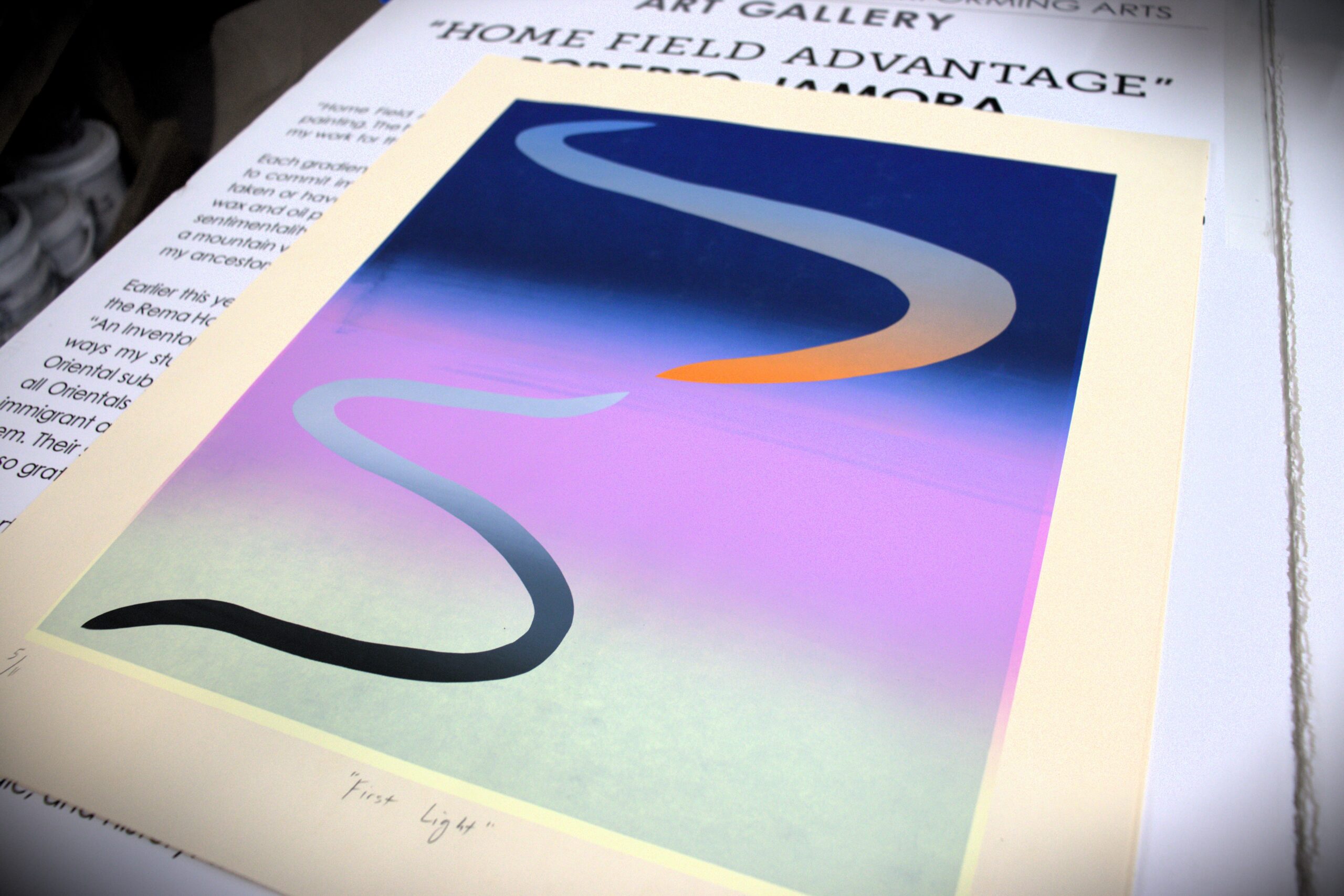 A colorful print titled "First Light" rests on an open portfolio.