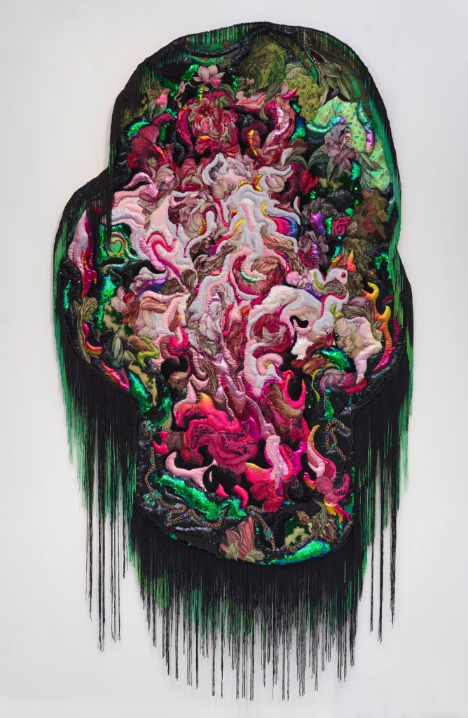 Varying pinks and reds, in multi-textured fabrics, swirl together surrounded by greens and fringe in green and black.