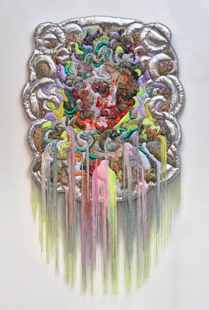 Curling and curving fabrics in multiple colors come together to form a woman's face. A silver shiny fabric is used around the edges of the image. Fringe at the bottom of image picks up primarily on the textile painting's light greens, pale pinks, and silver (which looks gray on the fringe).