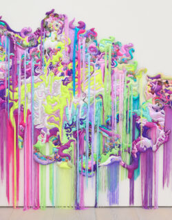 Textiles in a neon color palette (including greens, purple, and pinks) come together to form a woman. Fabrics include florals, sequins, and rainbow patterns. Fringe in various colors hangs down from both higher up the textile painting and the bottom of the textile art.