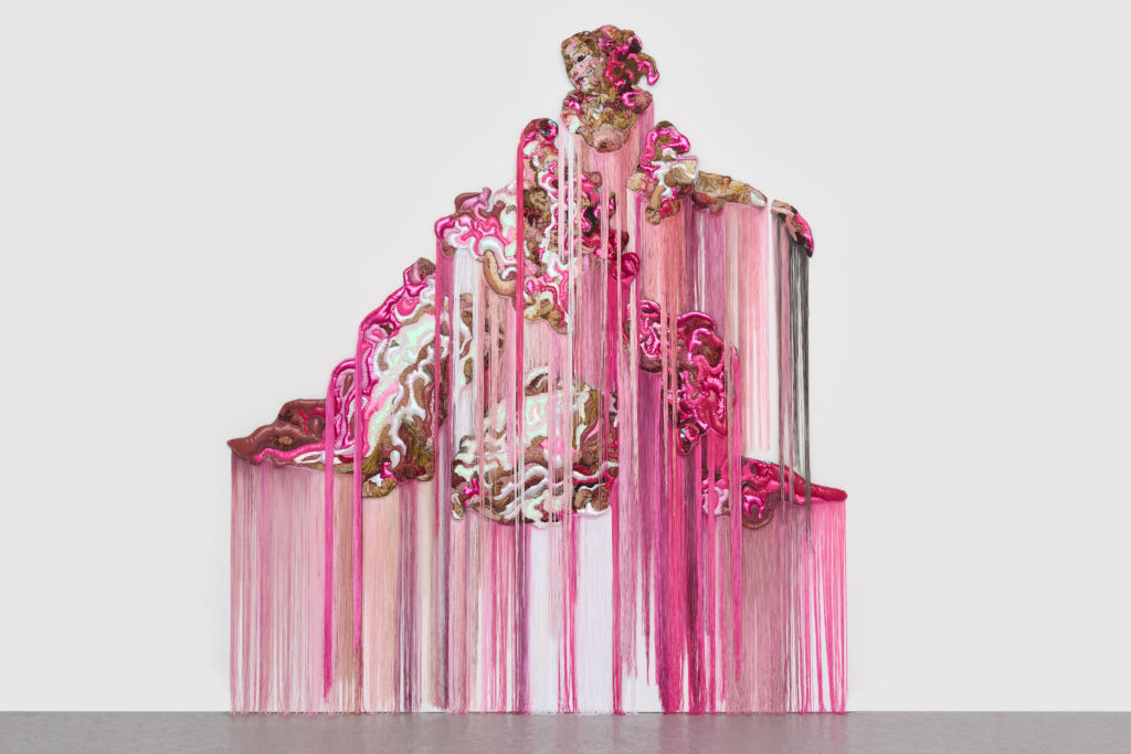 Pink and brown textiles of different textures come together to form a woman's face and dripping body, with fringe in browns and pinks.