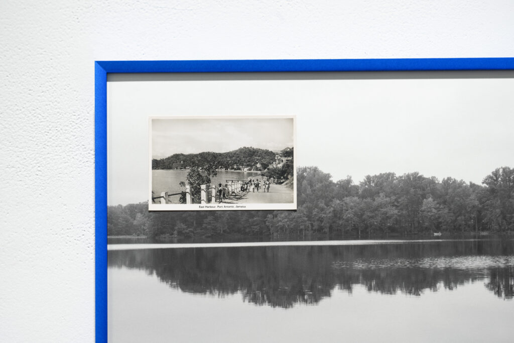 Close-up showing black-and-white postcard labeled "Easter Harbour, Port Antonio, Jamaica" showing people walking on path alongside water, placed on top of a black-and-white photo of water and trees