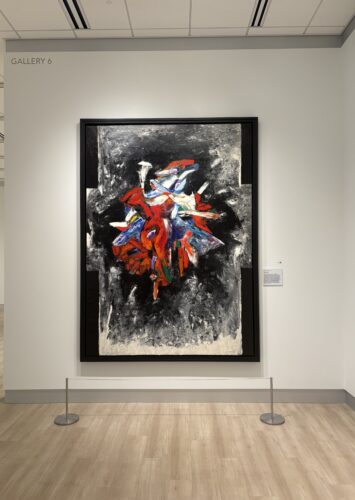 Abstract painting on white wall that says "GALLERY 6." Painting includes tangle of shapes with reds and blues surrounded by black and grays.