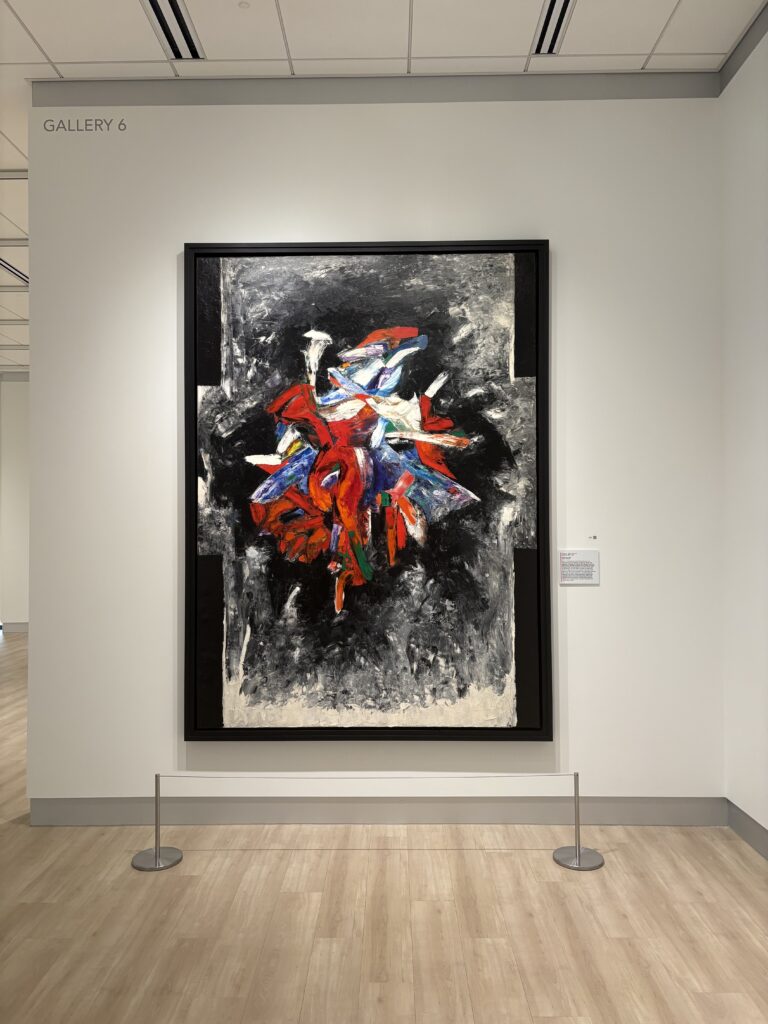 Abstract painting on white wall that says "GALLERY 6." Painting includes tangle of shapes with reds and blues surrounded by black and grays.