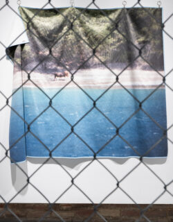 Close-up of beach landscape printed on towel through the holes in a chain link fence.